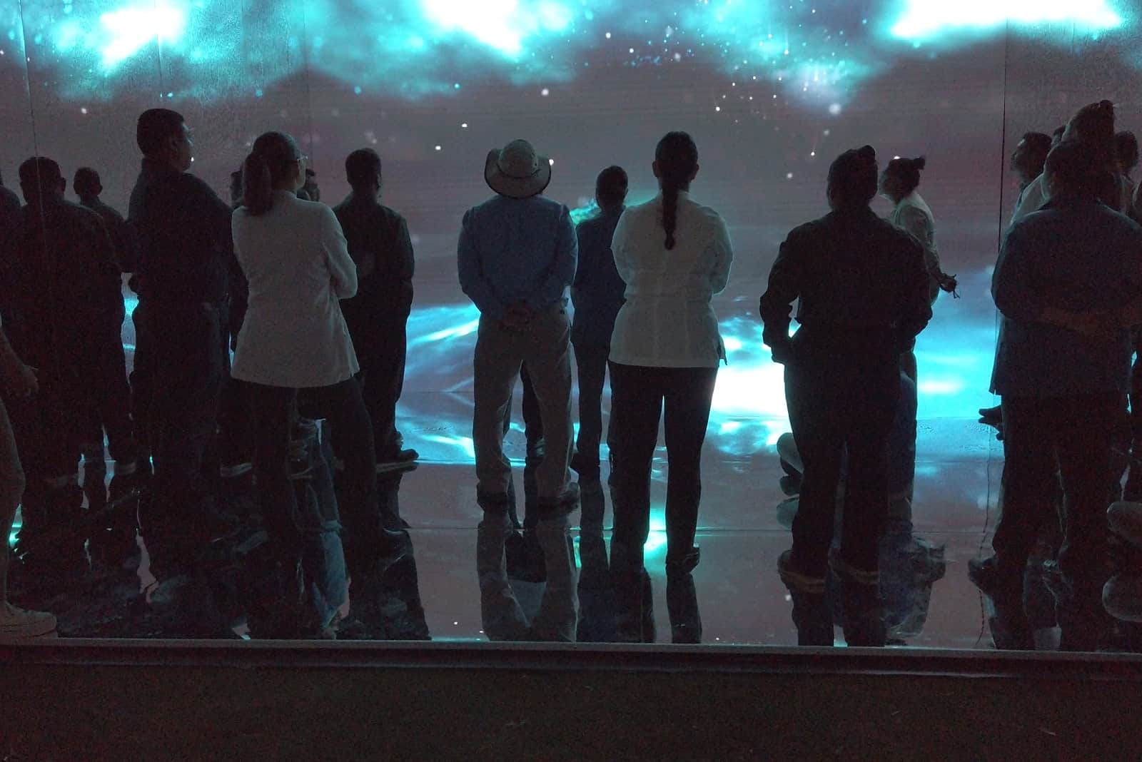Grupo de personas sobre un escenario observando atentamente una pantalla gigante con el video del espacio